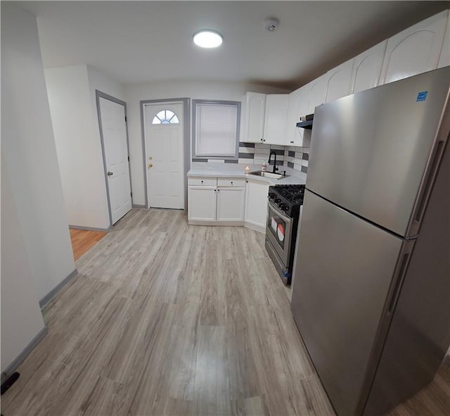 kitchen featuring stainless steel appliances, backsplash, white cabinets, light hardwood / wood-style flooring, and sink