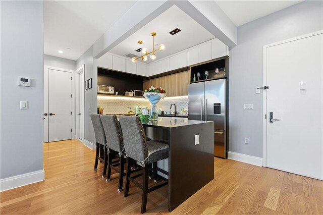 kitchen with high end refrigerator, light wood-type flooring, backsplash, sink, and a breakfast bar area