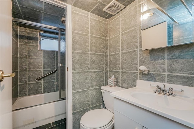 bathroom featuring tile walls, visible vents, toilet, enclosed tub / shower combo, and vanity