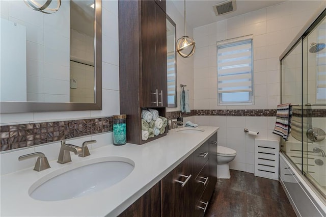 bathroom featuring toilet, a sink, visible vents, tile walls, and combined bath / shower with glass door