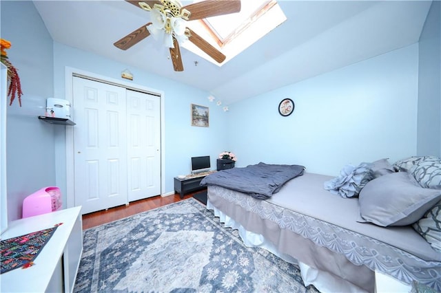 bedroom with a ceiling fan, vaulted ceiling with skylight, a closet, and wood finished floors