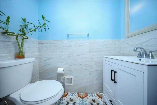 half bath with visible vents, vanity, toilet, and tile walls