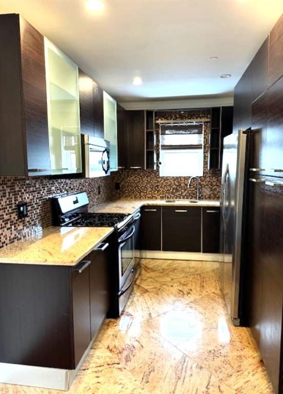 kitchen with sink, backsplash, dark brown cabinets, stainless steel appliances, and light stone countertops