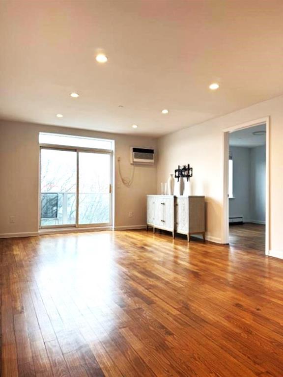 unfurnished living room featuring a baseboard radiator, wood-type flooring, and a wall unit AC