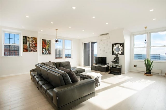 living room with a wall mounted air conditioner, light hardwood / wood-style flooring, and an inviting chandelier