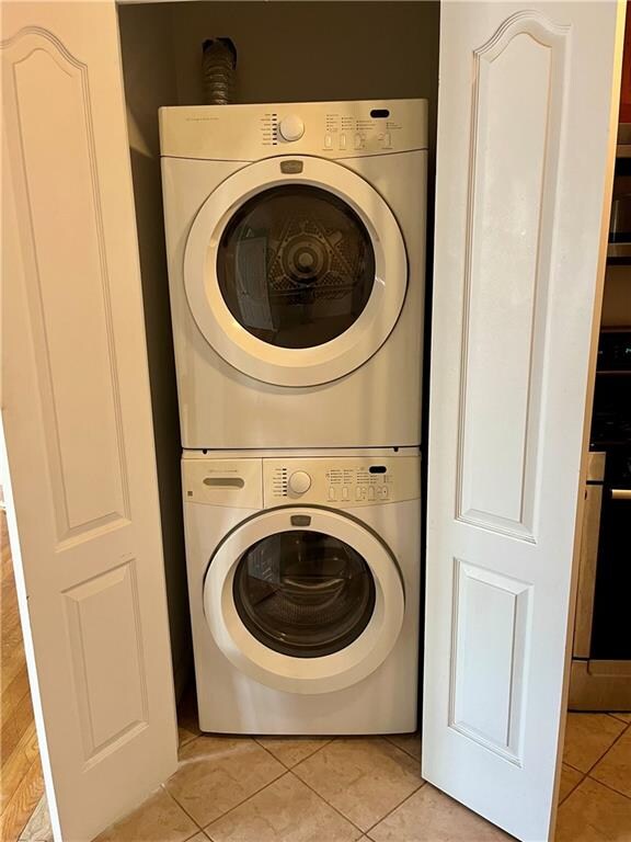 clothes washing area with light tile patterned floors, stacked washer / drying machine, and laundry area