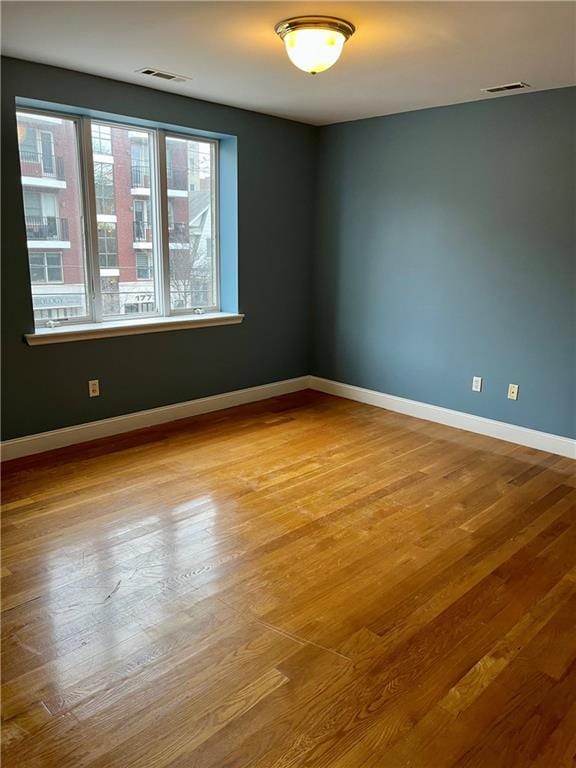 spare room featuring wood finished floors, visible vents, and baseboards