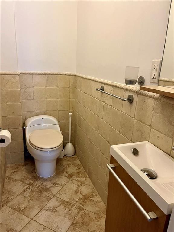 bathroom featuring toilet, tile walls, wainscoting, and vanity