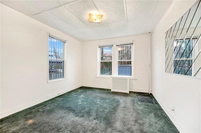 empty room with dark colored carpet, radiator, and a healthy amount of sunlight