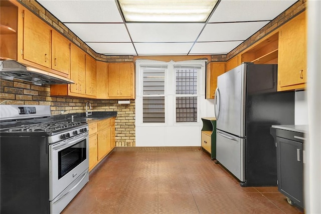 kitchen with sink, a drop ceiling, dark tile patterned floors, decorative backsplash, and appliances with stainless steel finishes