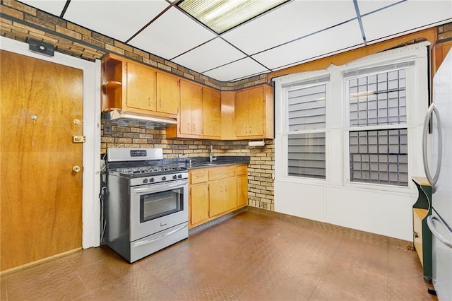 kitchen with sink, a drop ceiling, stainless steel gas range oven, white refrigerator, and backsplash