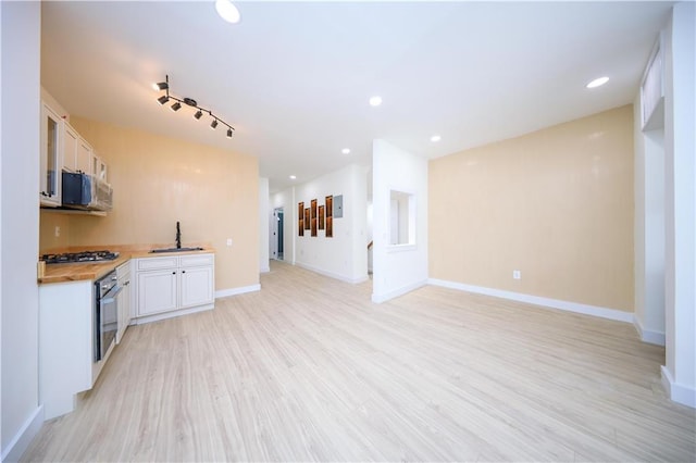 kitchen featuring sink, wood counters, light hardwood / wood-style flooring, stainless steel gas stovetop, and white cabinets