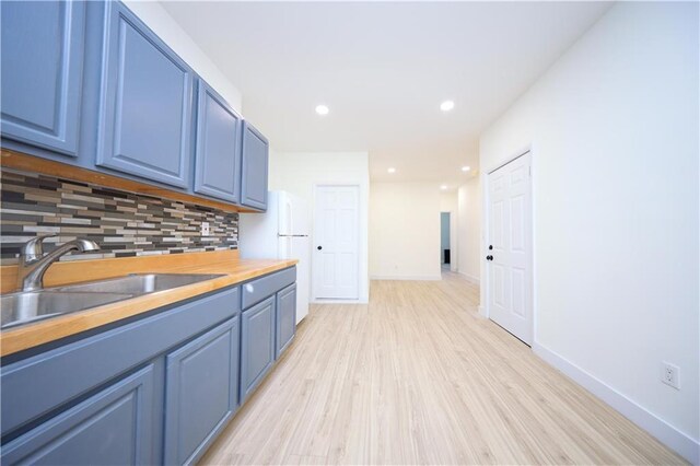 kitchen featuring light wood finished floors, backsplash, baseboards, blue cabinets, and a sink