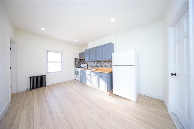 kitchen with light wood-type flooring, radiator heating unit, white appliances, light countertops, and decorative backsplash