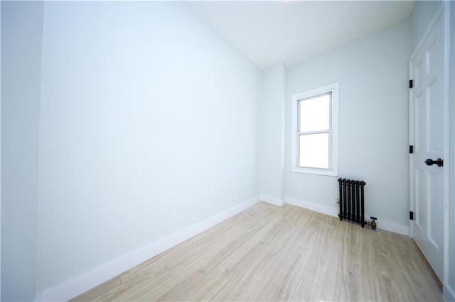 empty room featuring baseboards, light wood-style flooring, and radiator heating unit