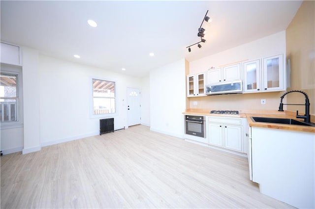 kitchen featuring appliances with stainless steel finishes, glass insert cabinets, light wood-style floors, and a sink