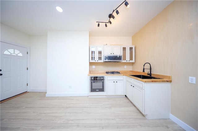 kitchen with light wood-style flooring, a sink, appliances with stainless steel finishes, light countertops, and glass insert cabinets