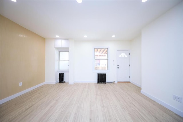 unfurnished living room with baseboards, light wood-style floors, and radiator heating unit