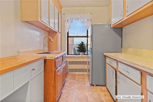 kitchen with light tile patterned flooring, sink, white cabinetry, radiator heating unit, and stainless steel fridge