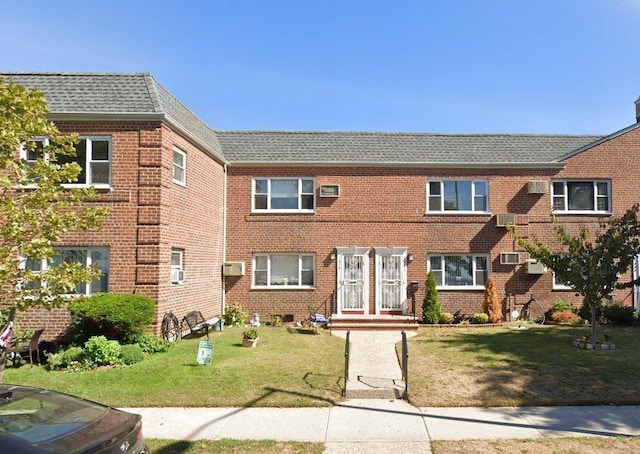view of property with a front lawn, brick siding, and a wall mounted AC