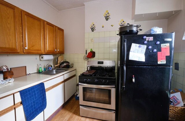 kitchen featuring black refrigerator, crown molding, sink, light hardwood / wood-style floors, and stainless steel range with gas stovetop