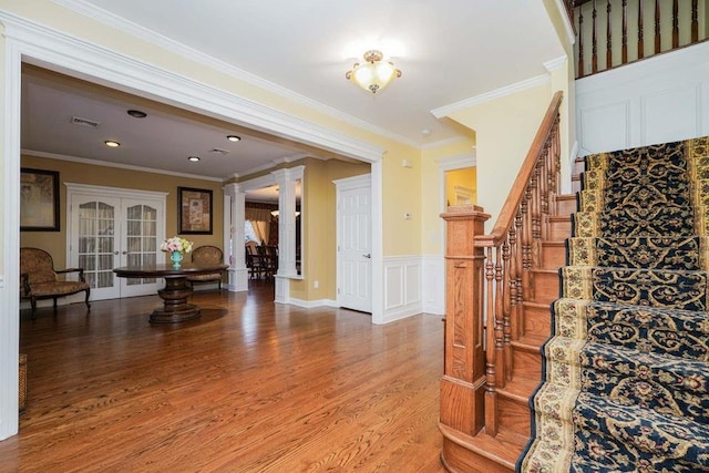 stairs with ornate columns, wood-type flooring, ornamental molding, and french doors