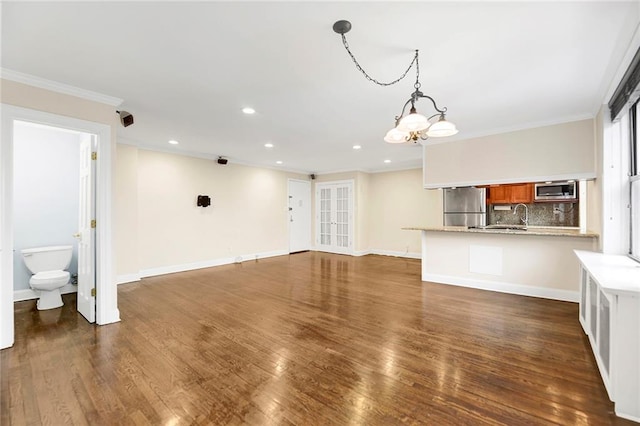 unfurnished living room featuring ornamental molding, dark wood-type flooring, a notable chandelier, and sink