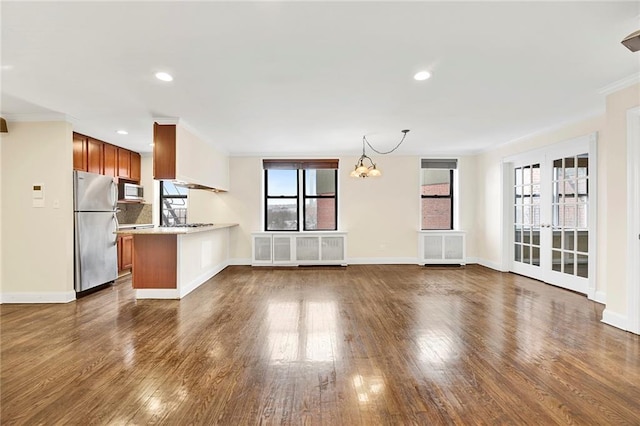 unfurnished living room featuring a notable chandelier, a healthy amount of sunlight, radiator heating unit, and dark hardwood / wood-style floors