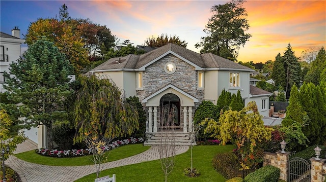 view of front of property with stone siding, a front yard, a gate, and stucco siding