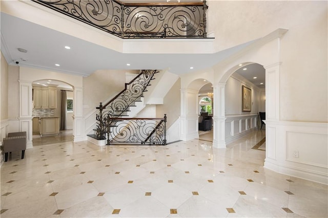 foyer entrance featuring a towering ceiling, ornate columns, plenty of natural light, and a decorative wall