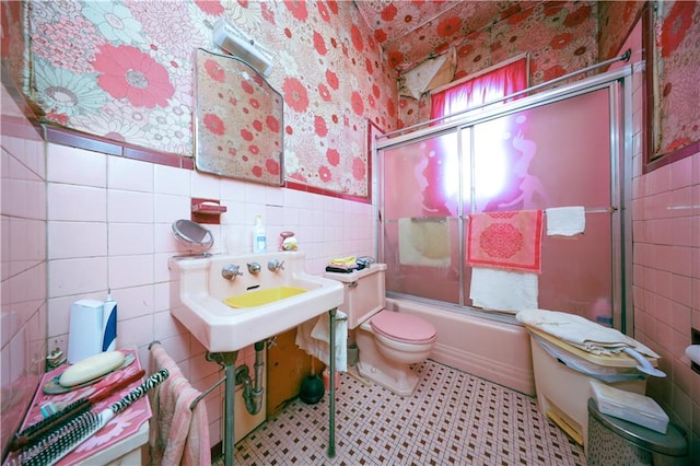 bathroom with tile walls, toilet, and combined bath / shower with glass door