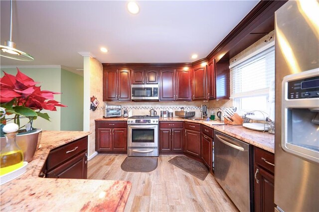 kitchen with ornamental molding, tasteful backsplash, light hardwood / wood-style flooring, hanging light fixtures, and appliances with stainless steel finishes