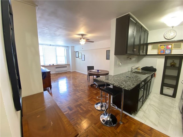 kitchen with radiator, sink, dark stone countertops, a kitchen bar, and light parquet flooring