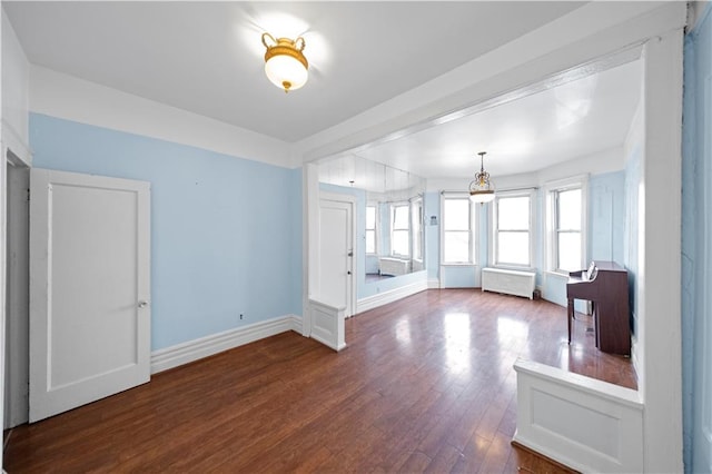 unfurnished living room featuring dark wood-style floors, radiator heating unit, and baseboards