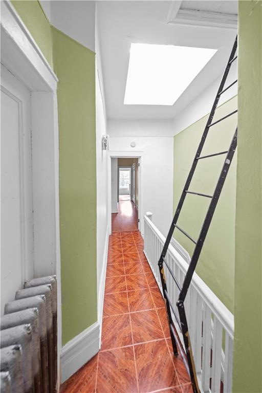 hall with tile patterned floors, a skylight, and baseboards