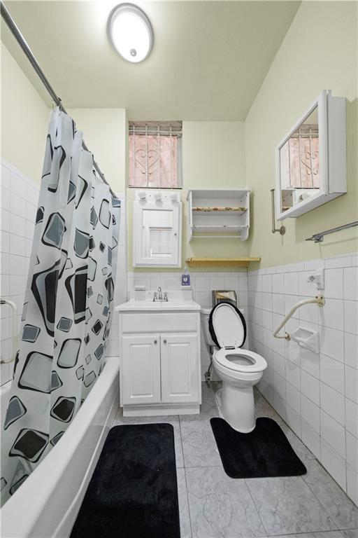 full bath featuring vanity, a wainscoted wall, shower / bath combo, tile walls, and toilet