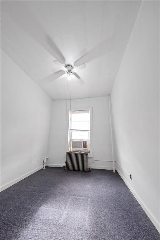 unfurnished room featuring radiator, baseboards, dark carpet, and ceiling fan