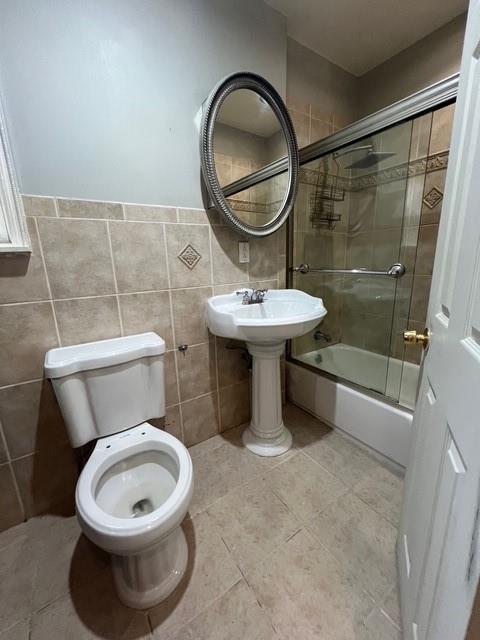 1241 E 98th St, Brooklyn, NY 11236 - full bathroom featuring combined bath / shower with glass door, toilet, tile walls, tile patterned floors, and wainscoting