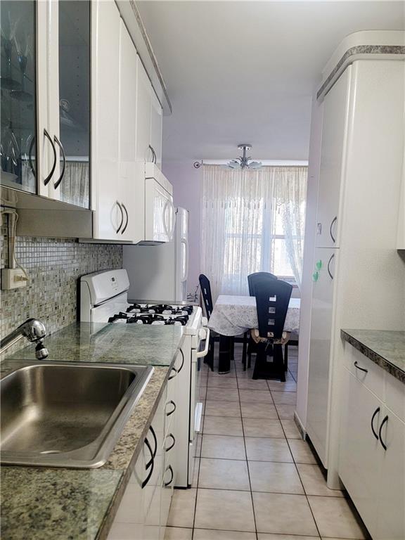 kitchen featuring light tile patterned flooring, tasteful backsplash, white cabinetry, sink, and white appliances