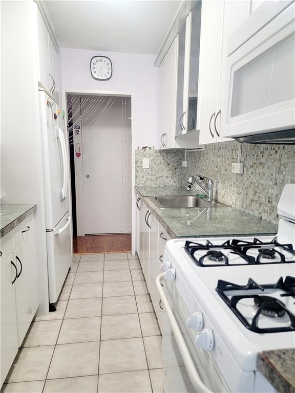 kitchen featuring white appliances, a sink, white cabinets, backsplash, and glass insert cabinets