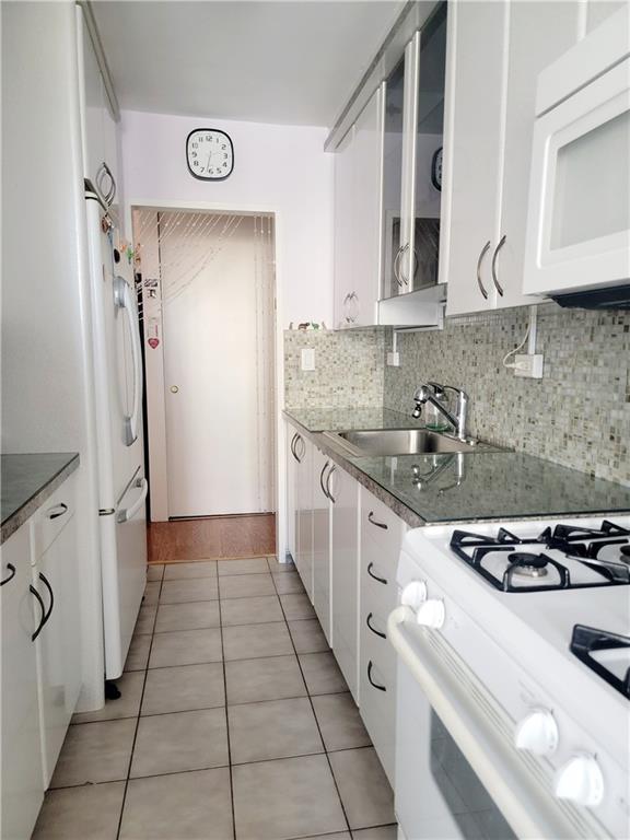 kitchen featuring white appliances, a sink, white cabinets, light tile patterned flooring, and tasteful backsplash