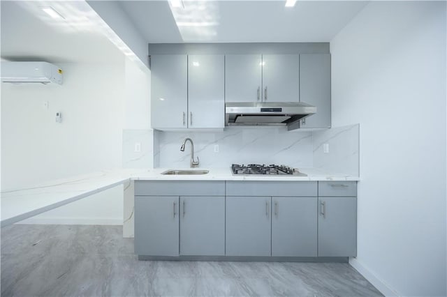 kitchen featuring light stone countertops, an AC wall unit, under cabinet range hood, stainless steel gas cooktop, and a sink