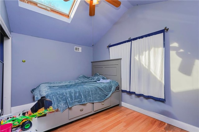 bedroom featuring vaulted ceiling with skylight, visible vents, baseboards, wood finished floors, and a ceiling fan