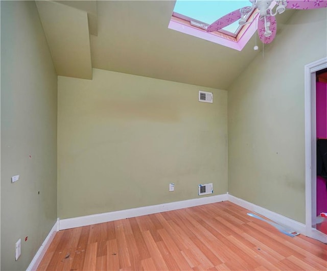 interior space featuring lofted ceiling with skylight, a ceiling fan, visible vents, and wood finished floors