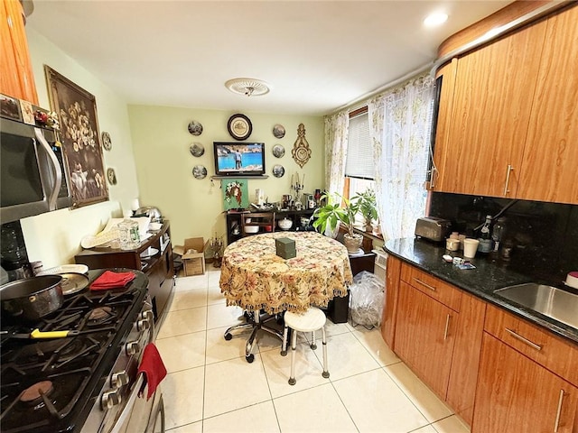 kitchen featuring sink, tasteful backsplash, dark stone counters, light tile patterned floors, and stainless steel appliances