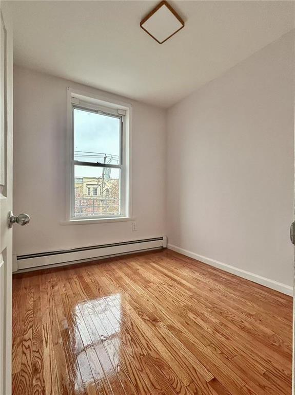 spare room featuring baseboard heating and light hardwood / wood-style floors