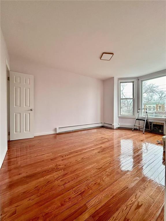 unfurnished living room featuring baseboard heating and hardwood / wood-style floors