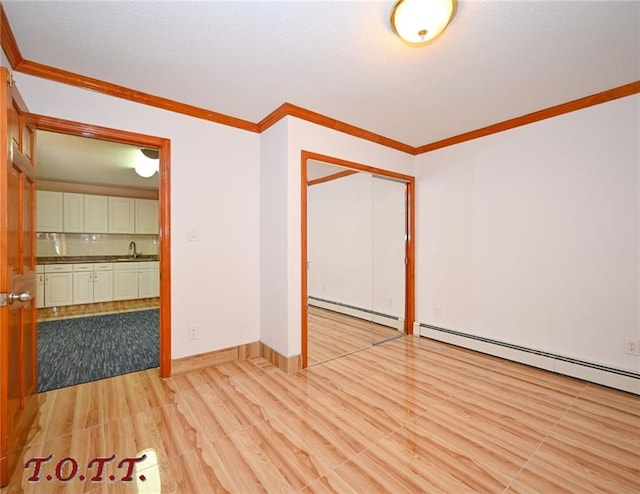 empty room with light hardwood / wood-style flooring, sink, crown molding, and a baseboard radiator