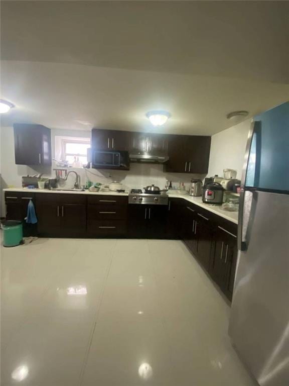 kitchen with stove, dark brown cabinetry, stainless steel refrigerator, and sink