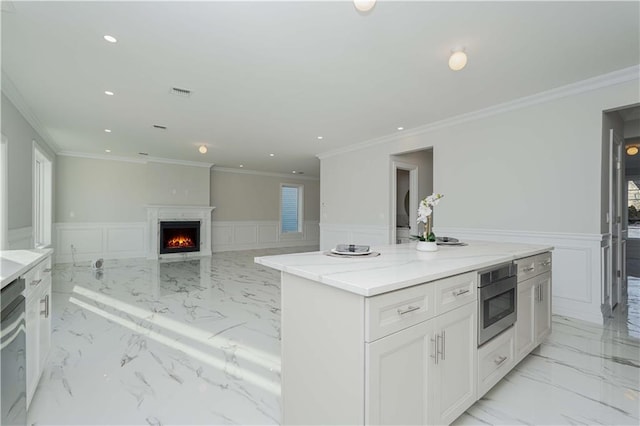 kitchen with light stone countertops, ornamental molding, white cabinetry, and a center island